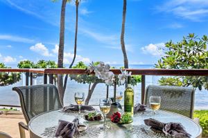 a table with wine glasses on a balcony with the ocean at Puunoa Beach Estates 205 in Lahaina