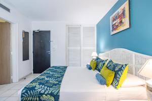 a bedroom with a white bed with yellow and blue pillows at Karibea Squash Hôtel in Fort-de-France