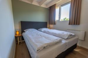 a bedroom with a bed with white sheets and a window at EuroParcs Cadzand-Bad in Cadzand