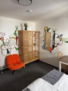 a bedroom with an orange chair and a wall with a painting at Hostel John Galt in Brno