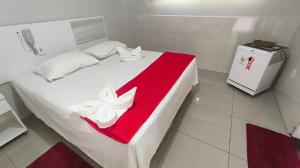 a white bed with a red and white towel on it at Hotel Senna in Arapiraca