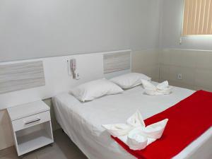 a white bed with a red blanket and white flowers on it at Hotel Senna in Arapiraca