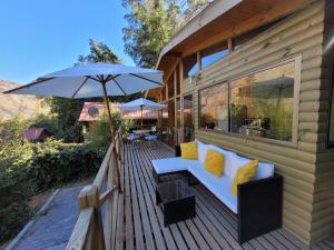 a wooden deck with a couch and an umbrella at Cabañas Carolín Cacao Castaño in San José de Maipo