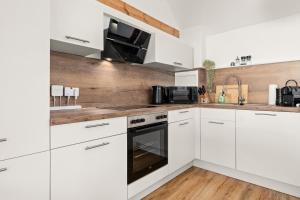 a white kitchen with white cabinets and wooden floors at KOLIBRI - Design Maisonette - Nintendo Switch, Streaming, Bikestore, E-Wallbox in Marburg an der Lahn