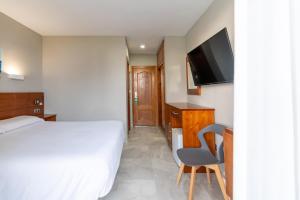 a bedroom with a bed and a chair and a television at Hotel Costa Azahar in Grao de Castellón