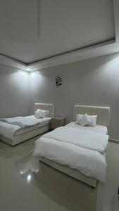 two beds in a white room with white sheets at شـقـة بغـرفـتـيـن Two rooms in Al Kharj