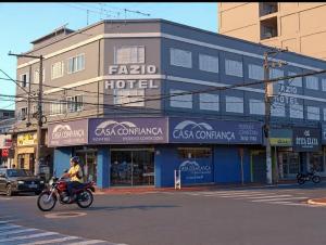 a man riding a motorcycle down a street in front of a building at Fazio Hotel in Jales