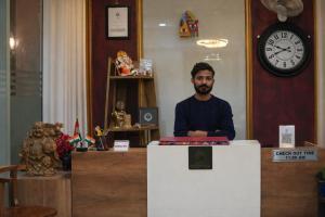 a man sitting at a counter in a room with a clock at Saffron Inn - Near India Expo Mart in Greater Noida