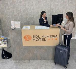 two women standing at a hotel counter with a suitcase at Hotel Sol Almería in Almería