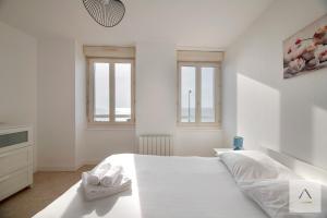 a white bedroom with a large white bed and windows at La Maison de Pêcheurs in Cancale