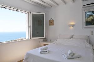 a white bedroom with a bed and a large window at La Maison Blanche in Agios Stefanos