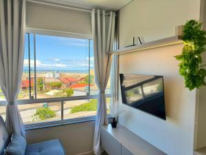 a living room with a tv and a large window at Apartamento com vista mar e perto da praia in Tramandaí