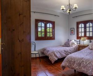 a bedroom with two beds and a chair and windows at El Cañaveral – Casa Rural con Terraza San Mateo in Vega de San Mateo