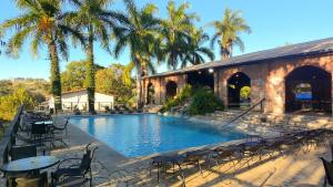 a swimming pool with chairs and tables and palm trees at Village Resort All Fun Inclusive in Jaboticatubas