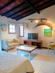 a room with a bed and a table and a tv at Palmares, Casa Rustica Suites Buzios in Búzios