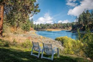 two chairs sitting in the grass next to a river at Private Riverfront Estate with Kayaks & Views in Post Falls