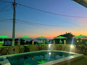 a swimming pool with green umbrellas and a sunset at Pousada & Espaço Orlla 39 in Maricá