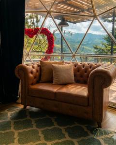 a brown couch in a room with a large window at Omghat Glamping - Domo Ganesha in El Peñol