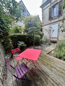 a red table and two chairs on a wooden deck at L'Escale à Villerville in Villerville