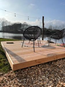 Zwei Stühle stehen auf einer Holzterrasse in der Nähe eines Sees. in der Unterkunft PipowagenTwente t huuske in Lattrop + 11 Fotos
