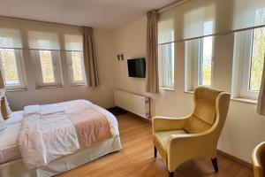 a bedroom with a bed and a chair and windows at Boutique Hotel Restaurant Hollerather Hof in Hellenthal