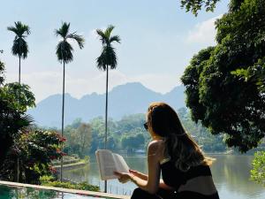 a woman reading a book while looking out at a lake at Maisonson Resort in Dương Kê