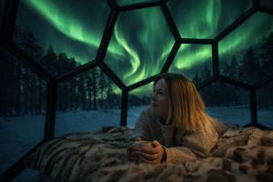 a woman laying in bed with a cup in her hand at SKOG Aurora Glass Igloos in Kalix +68 photos
