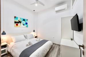 a white bedroom with a bed and a flat screen tv at Central Suites Aegina 2 in Egina