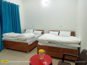 two beds in a room with a red table with a glass at Hukkam Homestay in Barkot