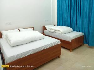 two beds in a room with blue curtains at Hukkam Homestay in Barkot