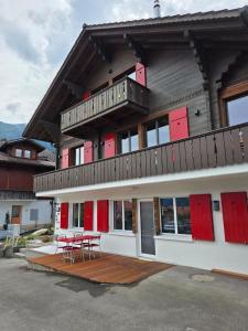 a building with red doors and two tables on a deck at Modernes Apartment - Lakeview Sunnmatte in Leissigen