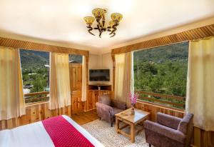 a bedroom with a bed and two chairs and windows at Manali Golden Valley in Manāli +16 photos