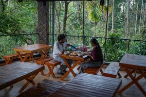 two people sitting at a wooden table on a deck at Kashmeeram Vythiri Wayanad Premium Pool Resort in Vayittiri