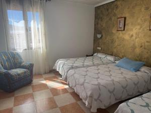a hotel room with two beds and a chair at Hostal Cabañas in Carboneras de Guadazaón