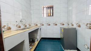 a white tiled bathroom with a sink and a refrigerator at Reine Hôtel in Bohicon