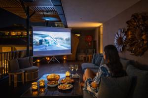 a woman sitting in a living room watching a car on a screen at Amaaranth Goa in Varca