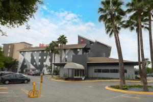 a building with palm trees in a parking lot at Ibis Monterrey Aeropuerto in Monterrey