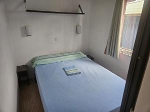 a small bedroom with a blue bed with a window at Camping Arenas in Bareyo