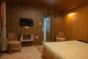 a bedroom with a bed and two chairs and a tv at Trippers CastleWoods in Darjeeling