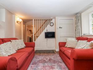 a living room with red couches and a tv at Yew Tree Cottage in Dartmouth