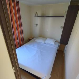 a small bedroom with a white bed with two pillows at Camping Lac aux Oiseaux - Mobil-home 3 Pièces 4 Personnes MAE-0991 in Martiel