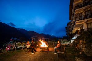 a group of people sitting around a fire at night at Hotel SNAS Retreat Manali in Manāli
