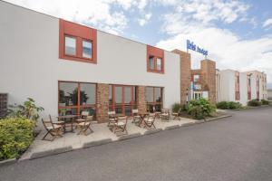 un bâtiment avec des chaises et des tables devant lui dans l'établissement ibis budget Rennes Chantepie, à Chantepie