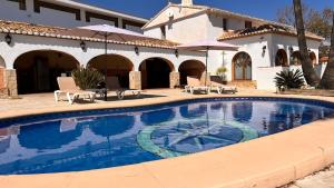 a swimming pool with chairs and umbrellas next to a house at Villa con piscina y barbacoa en Calpe in Calpe