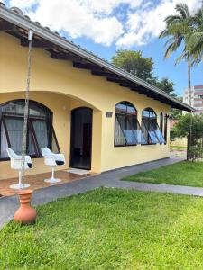 a yellow house with two white chairs in the yard at Econômica Joinville Hostel e Pousada in Joinville