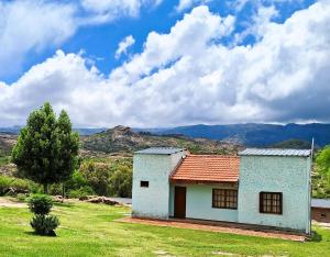a small house in a field with mountains in the background at Cabañas El Refugio de Juan in Mina Clavero