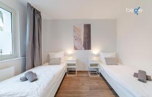 two beds in a room with white walls and wooden floors at BEGE APARTMENTS SmileStay in Gelsenkirchen