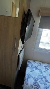 a small bedroom with a bed and a television at Serena Little Escape, West Sands Holiday in Selsey