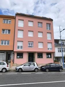 two cars parked in front of a pink building at Apartamento Sandy - wifi, ascensor, vistas al Mar,Amplio y Acogedor in Laxe