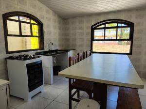 a kitchen with a table and a stove and two windows at Oásis - Casa com Piscina e Churrasqueira in Pontal do Paraná